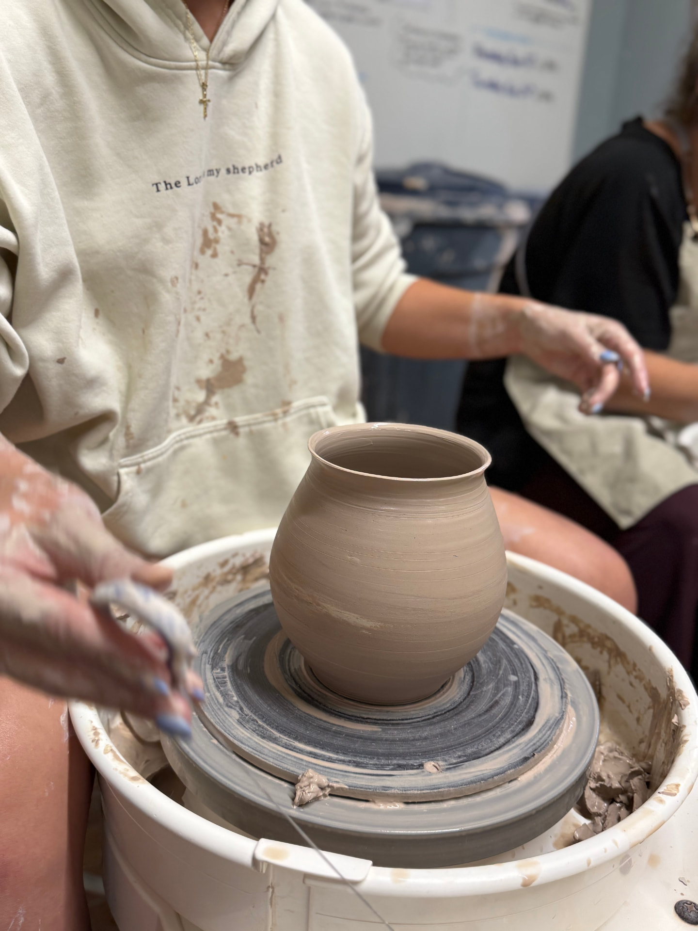 Jules at the wheel with clay on her hands, opening up a fresh pot