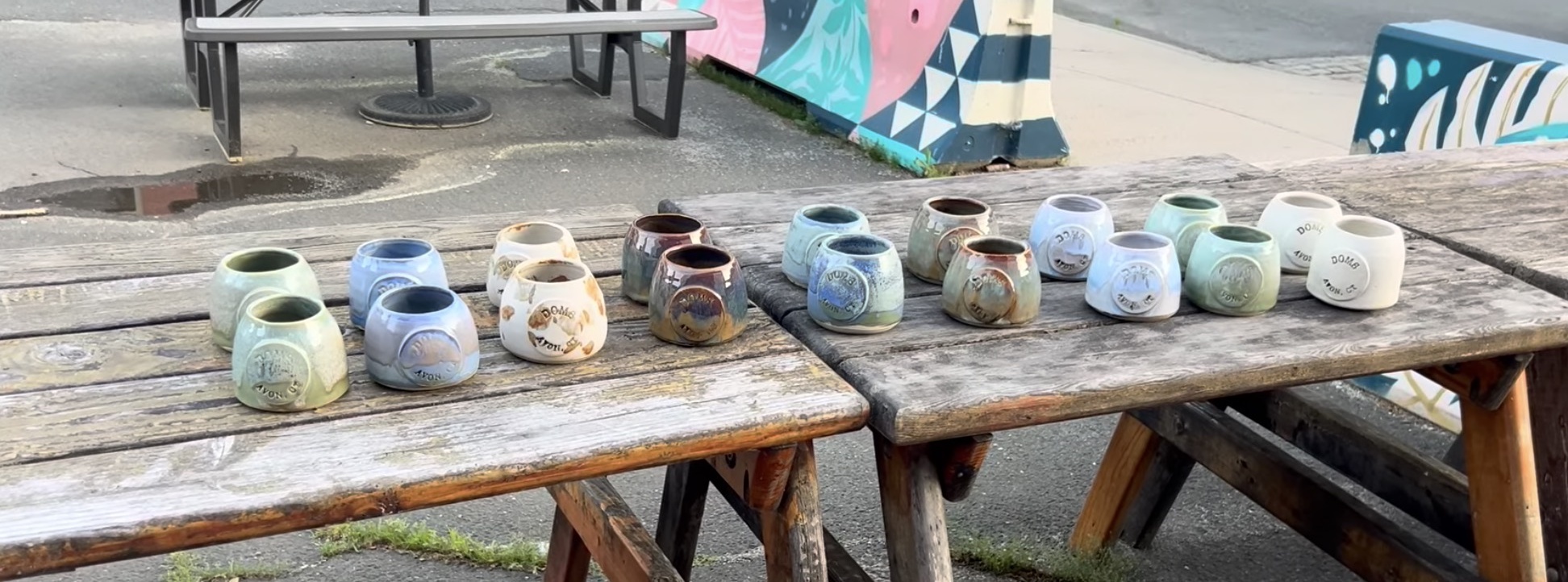 Handmade ceramic mugs lined up on a wooden picnic table for a wholesale order