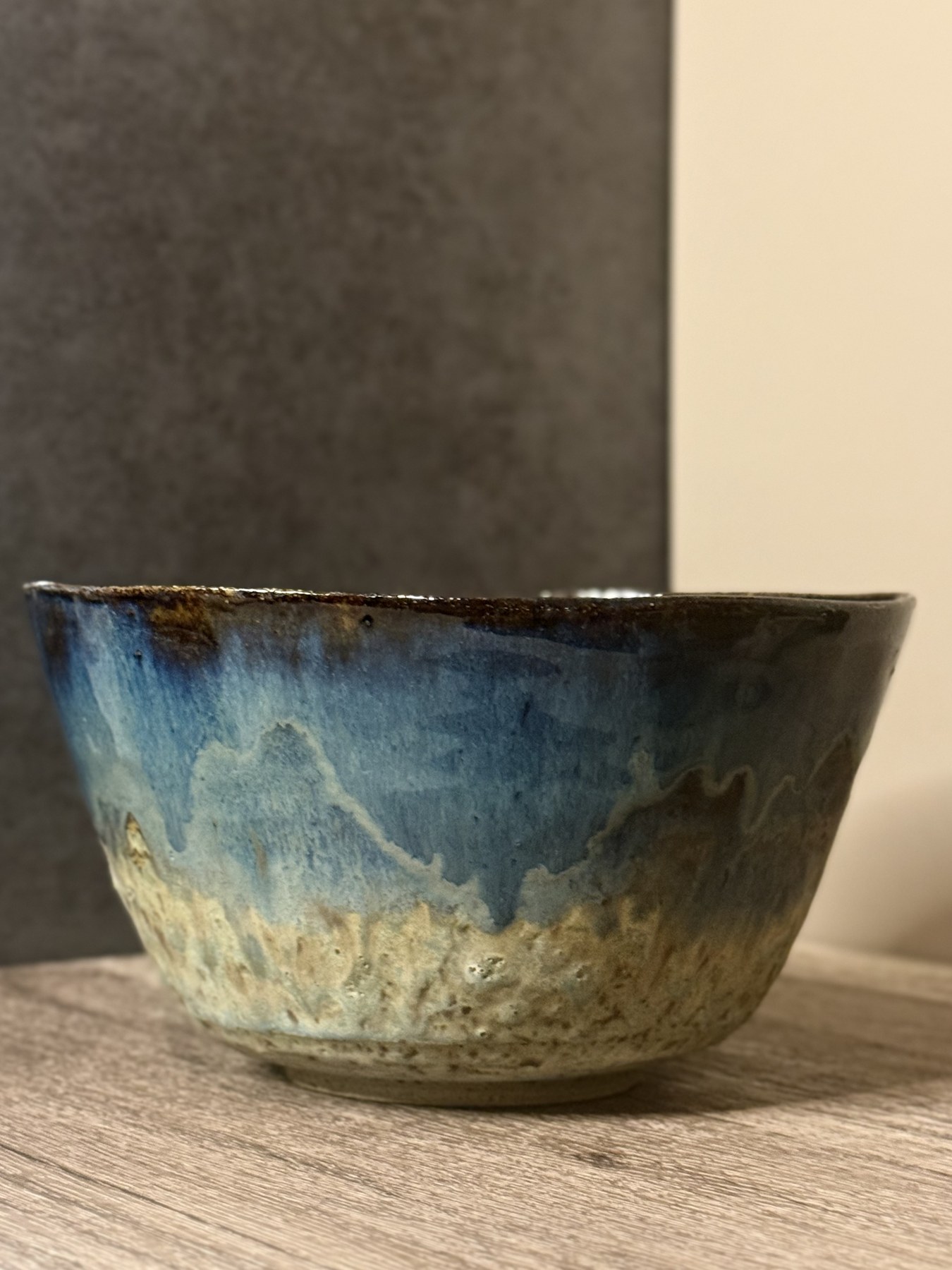 Handmade Drifted Seas Bowl with deep blue glaze drifting into sandy textured stoneware on a wooden table