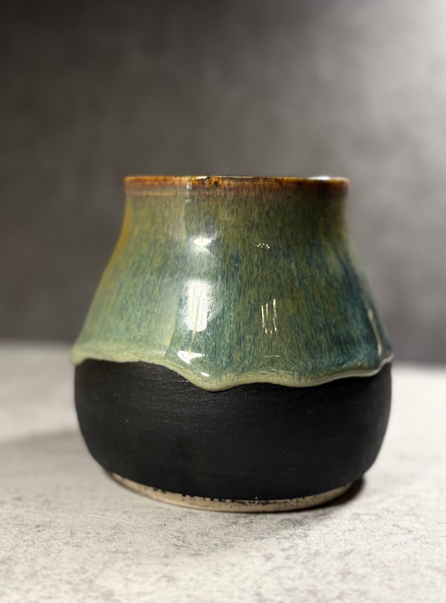 Rounded black clay vase with green tea and tiger's eye glaze dripping over the shoulder