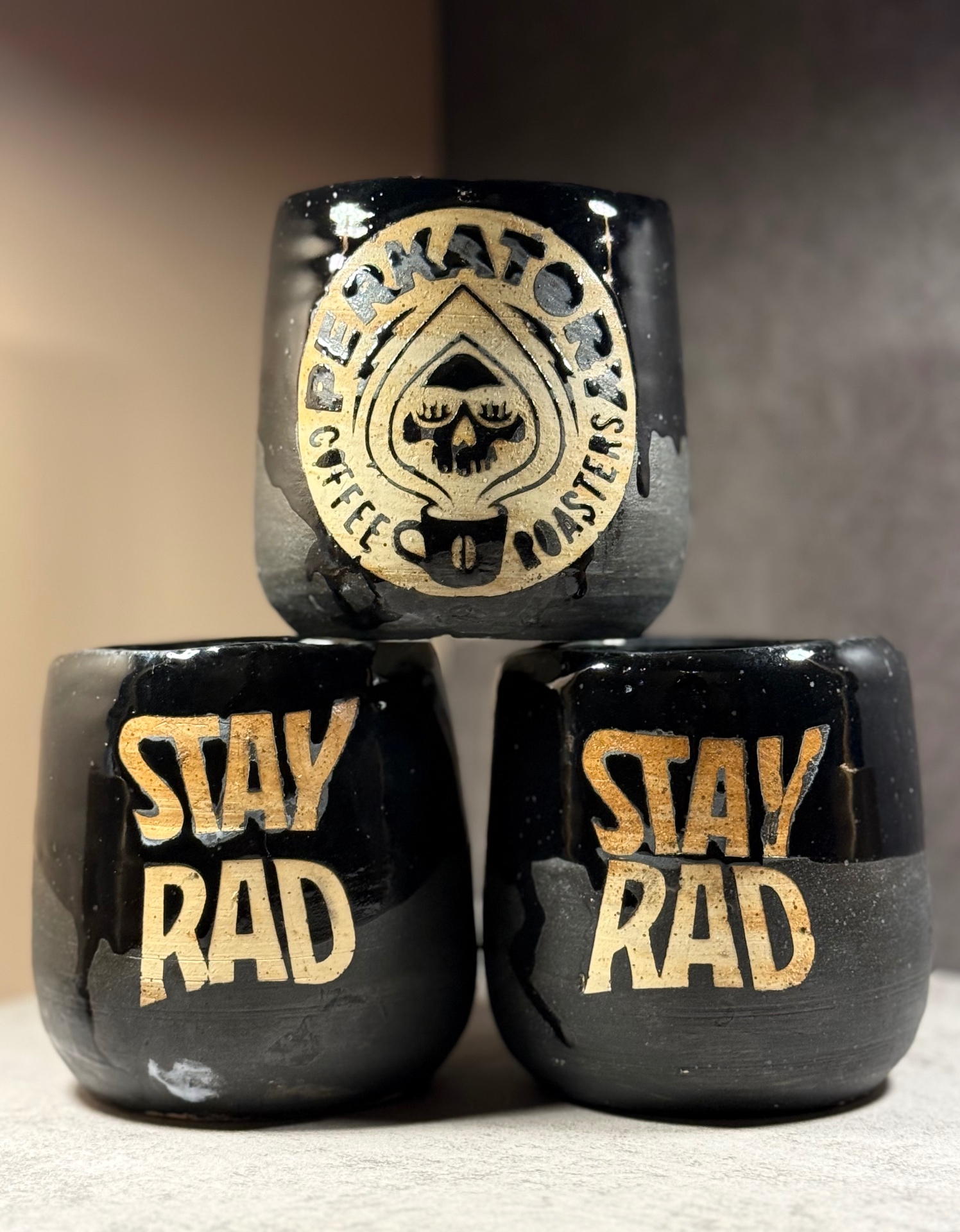 Stack of black Perkatory Coffee Roasters wholesale mugs with Stay Rad lettering