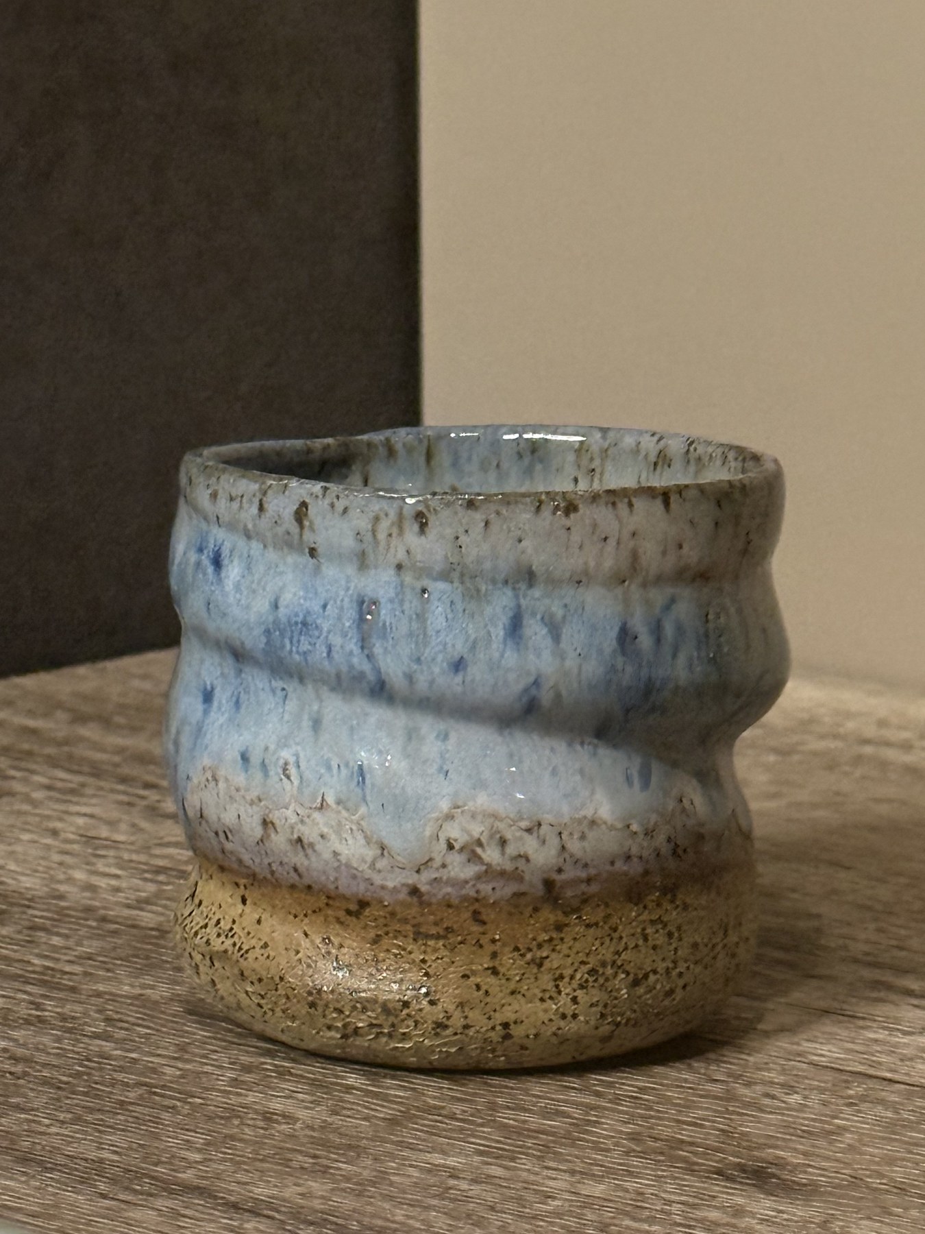 Wavy handmade tumbler with pale blue glaze and deeper blue flecks over speckled tan clay
