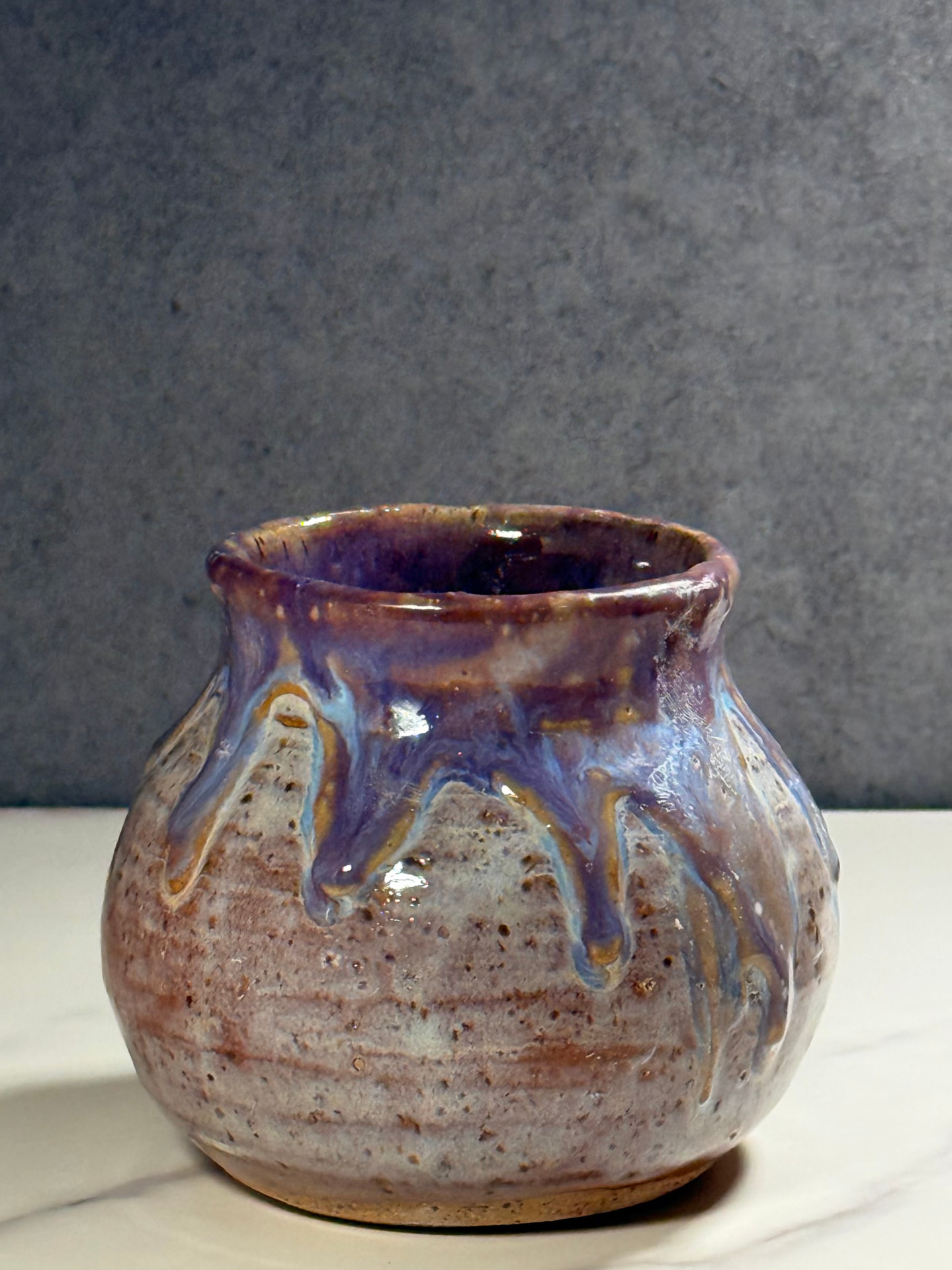 Small round vase with violet and blue glaze dripping over speckled clay