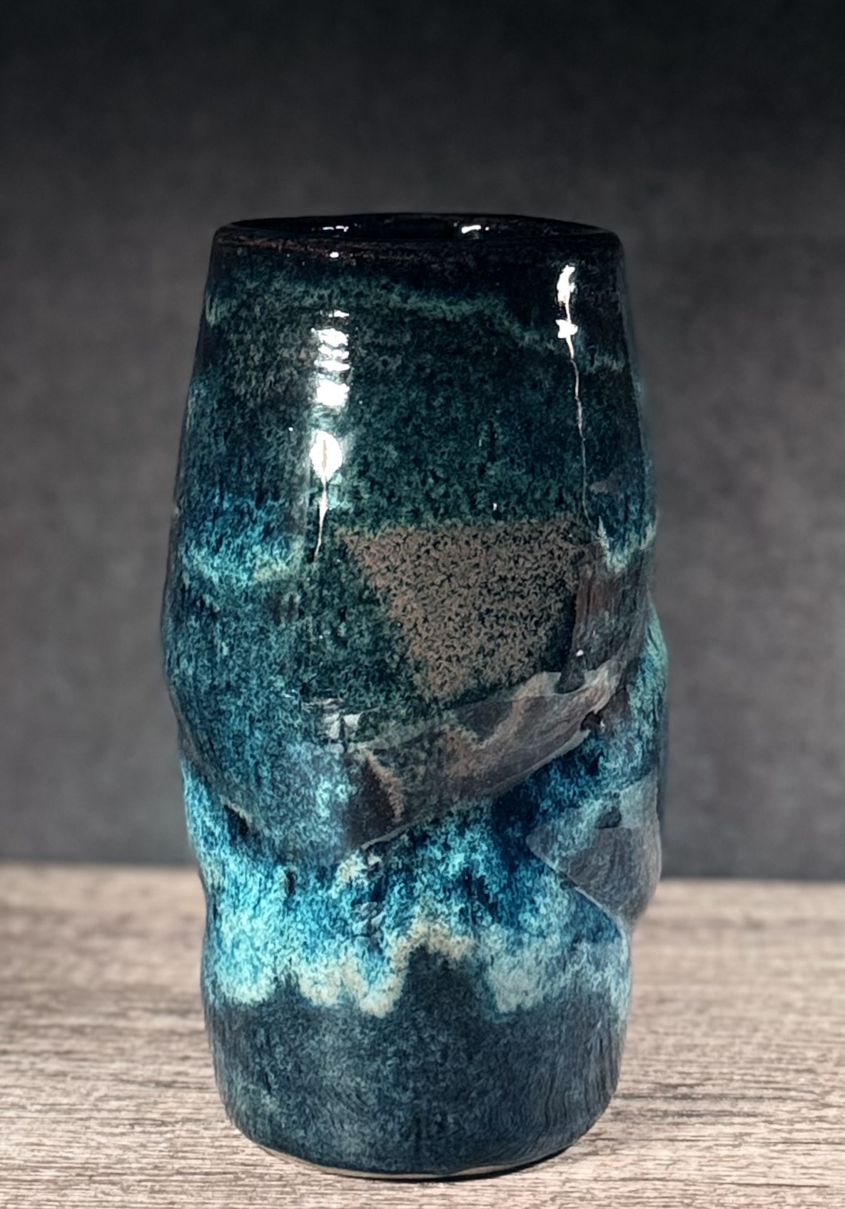 Tall handmade ceramic vase with deep blue and teal glaze on a wooden table