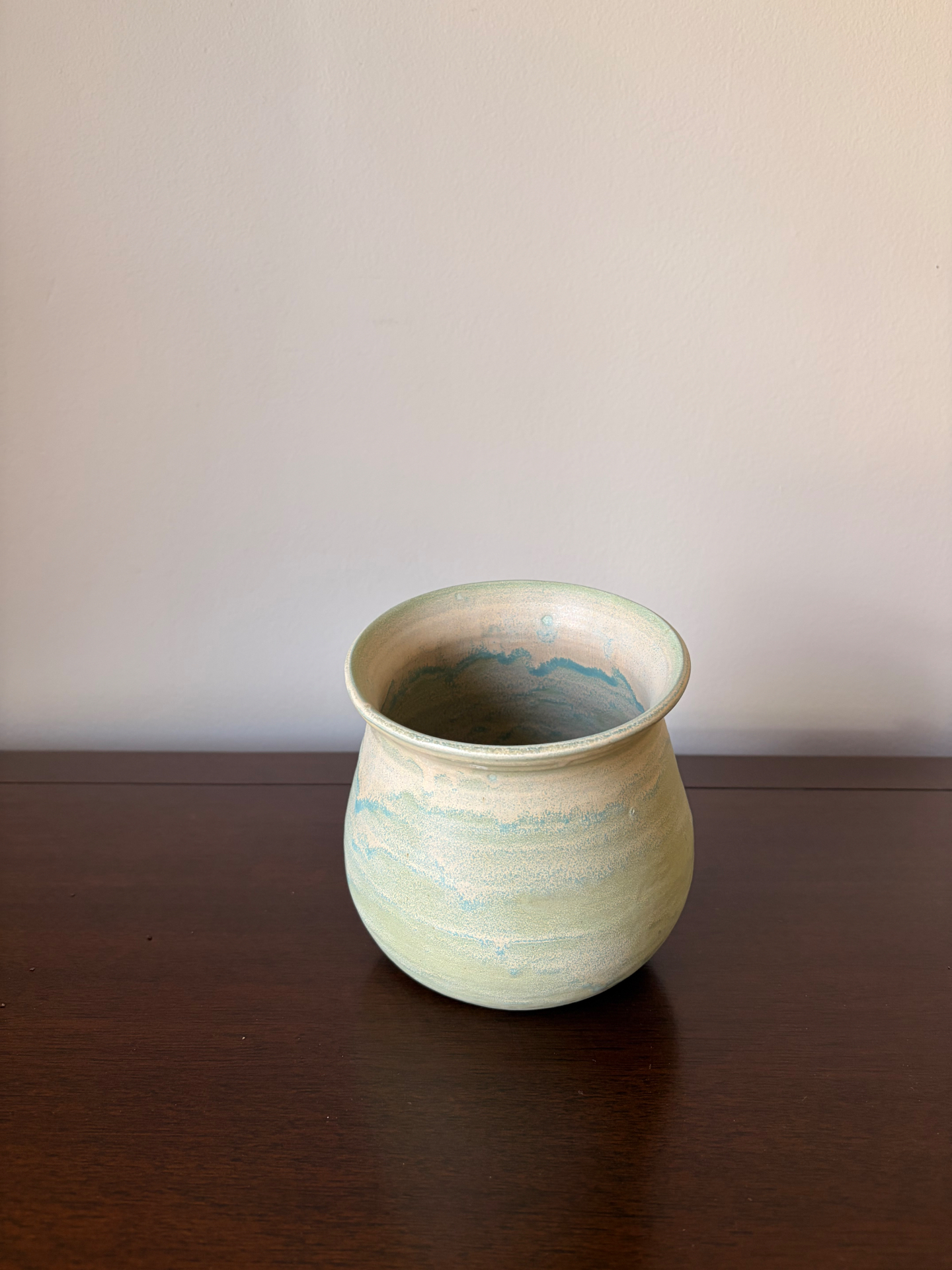 Round ceramic jar in pale seafoam green glaze over sandy cream clay on a dark wood table